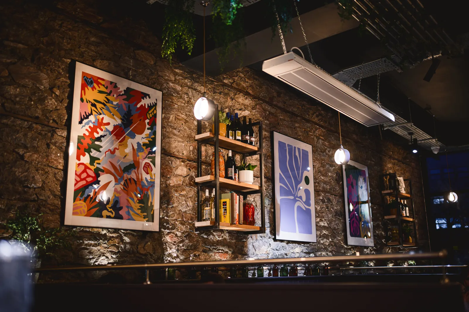 Exposed stone wall with colourful prints and shelves of natural wine at NORA'S